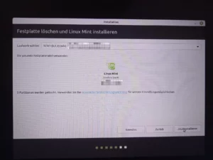 Foto von einem Bildschirm. Ein Installation Programm ist zu sehen mit dem Titel: Festplatte löschen und Linux Mint installieren. Das grüne Logo von Linux Mint ist in der Mitte zu sehen.